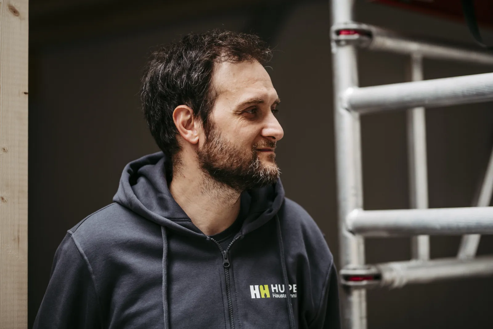 Mitarbeiter im Hupe-Hoodie vor einem Gerüst, Blick zur Seite